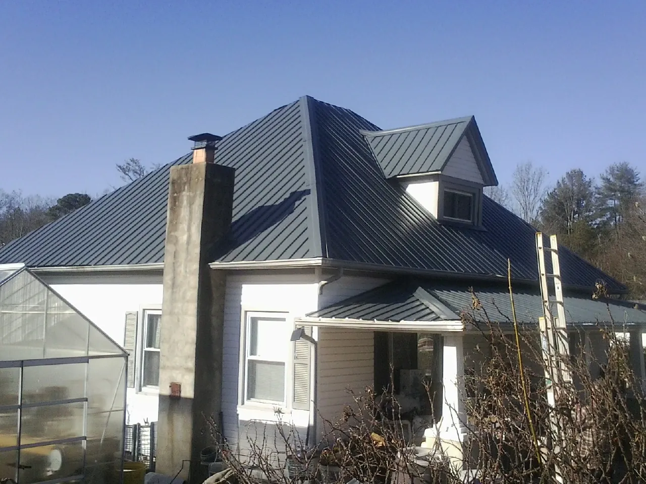 Dark blue standing seam metal roof on a white farmhouse with dormer — Slate & Tile Roof Repair by Roofing Brothers in Bloomington Springs