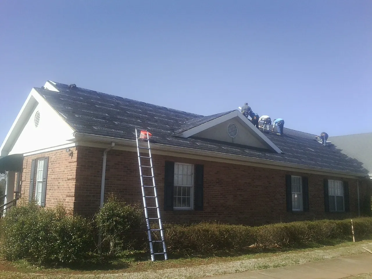 Crew tearing shingles off a brick ranch roof with a ladder set — Emergency Roof Repair work by our crew in Bloomington Springs