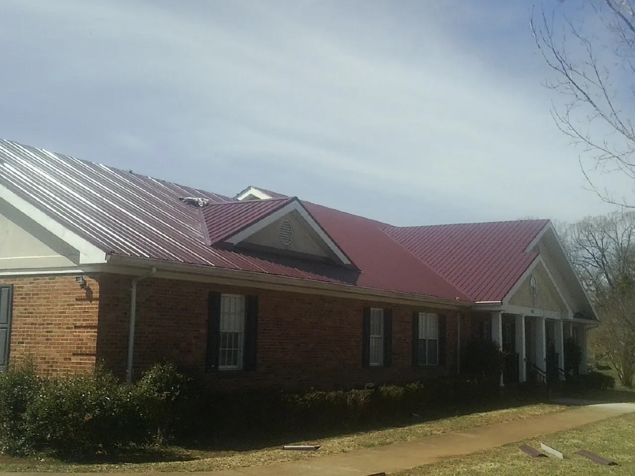 Red metal roof with gabled entries on a long brick building, from a Hail Damage Roof Repair job in Bloomington Springs