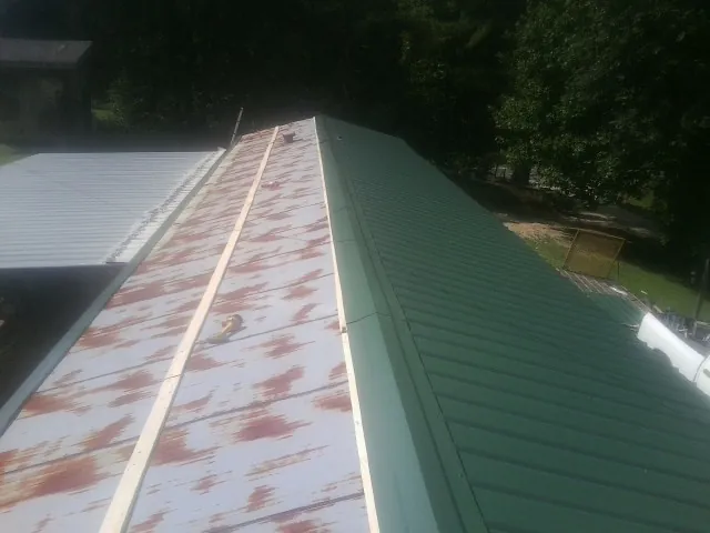 Old rusted panels beside newly installed green metal roofing — Wind Damage Roof Repair by Roofing Brothers in Bloomington Springs