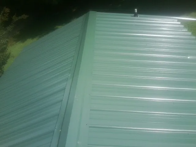 New green metal panels meeting at the ridge of a roof — Flat Roof Repair work by our crew in Bloomington Springs