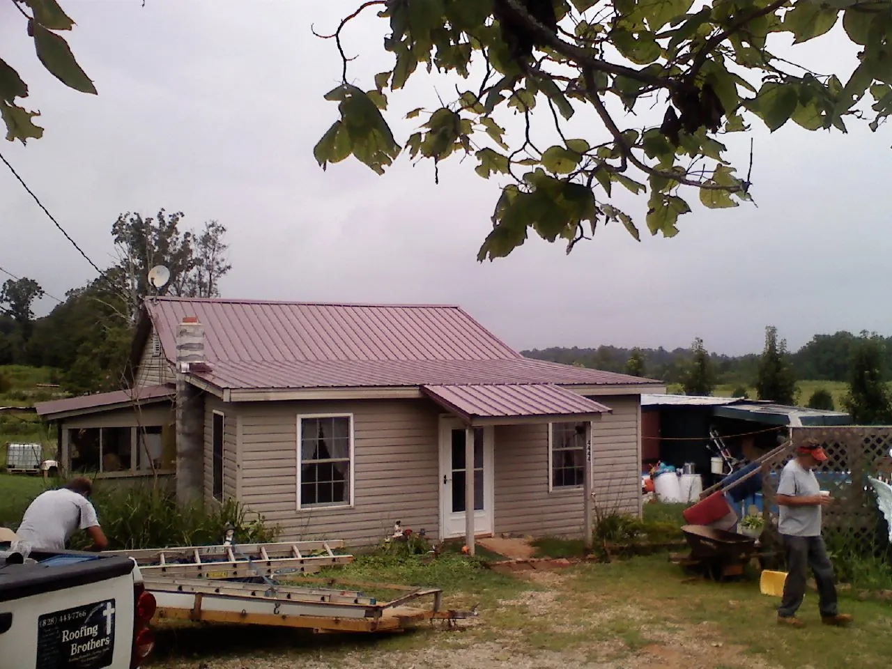 Crew finishing a mauve metal roof on a small farmhouse in Bloomington Springs