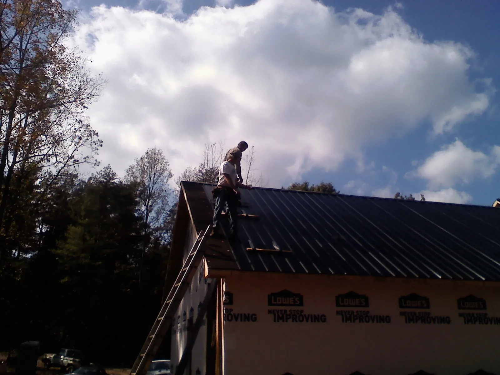 Roofer fastening dark metal panels high against a cloudy sky, from a Roof Inspection job in Bloomington Springs