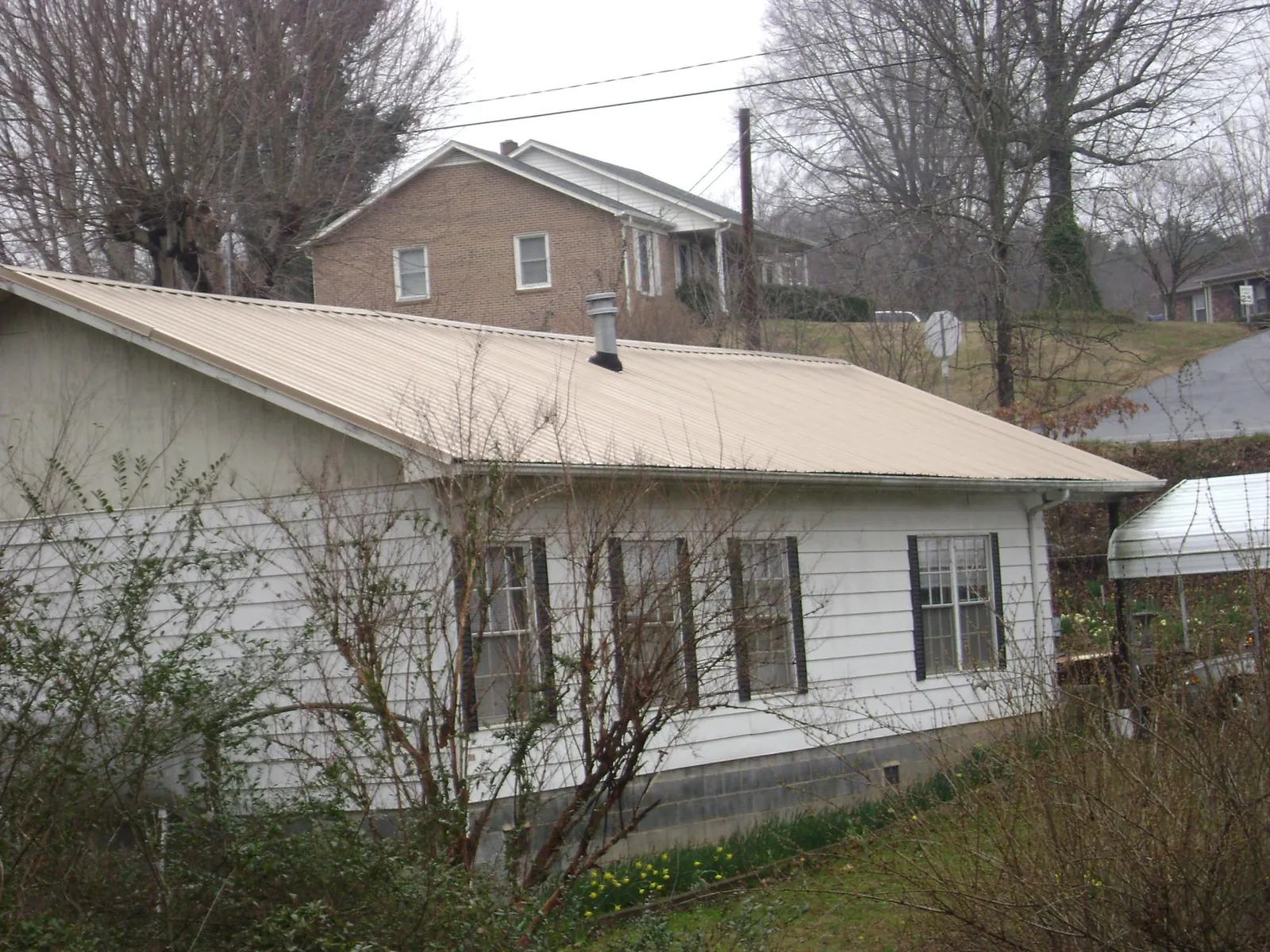 Tan metal roof on a white sided house set into a hillside — Commercial Roofing by Roofing Brothers in Bloomington Springs