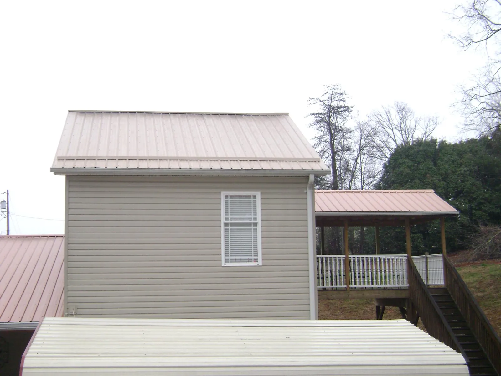 Tan metal roofs on a two story addition and attached porch, from a Roof Replacement job in Bloomington Springs